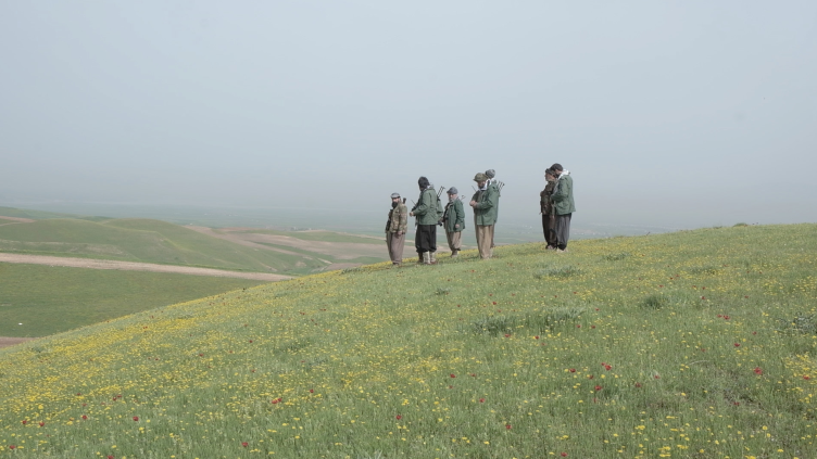 Vier Personen stehen auf einem grünen Hügel in einer nebligen Landschaft.